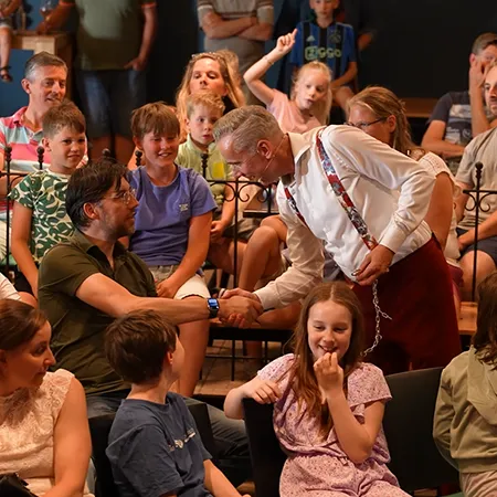 Goochelaar Jan Smulders schudt de hand van een vader in het publiek tijdens een interactieve familieshow op een Molecaten park.